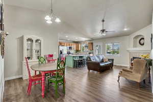 Dining area with dark wood-style flooring, a fireplace, baseboards, ceiling fan with notable chandelier, and vaulted ceiling