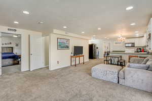 Living area featuring light carpet, recessed lighting, and a notable chandelier