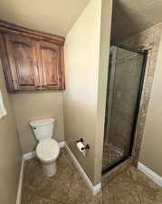 Bathroom featuring a textured ceiling, baseboards, tile patterned floors, and a stall shower