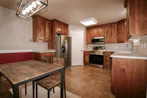Kitchen with brown cabinets, a sink, light countertops, light tile patterned floors, and stainless steel appliances
