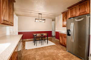 Kitchen featuring brown cabinets, a sink, stainless steel fridge with ice dispenser, a textured ceiling, and decorative light fixtures