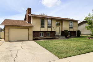 Split foyer home with an attached garage, a front lawn, brick siding, a chimney, and driveway