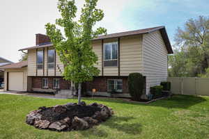 Bi-level home with an attached garage, a gate, a front lawn, and a chimney