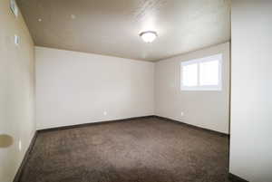 Carpeted empty room featuring a textured ceiling and baseboards