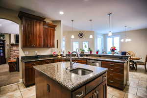Kitchen featuring a sink, dark stone counters, dishwasher, and a center island with sink