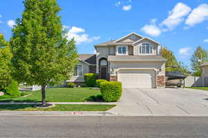 Traditional-style home featuring a garage, driveway, a front lawn, and stucco siding