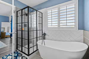 Bathroom featuring wainscoting, french doors, tile walls, a soaking tub, and a stall shower