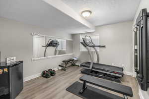 Exercise room featuring baseboards, a textured ceiling, and wood finished floors