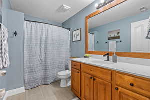 Full bathroom with toilet, a textured ceiling, visible vents, and vanity