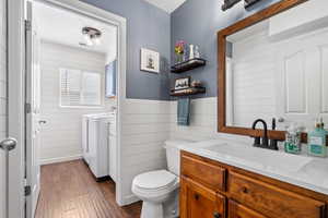 Bathroom with wood finished floors, vanity, toilet, wooden walls, and washer and clothes dryer