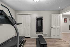 Exercise area with light wood-style floors, baseboards, and a textured ceiling
