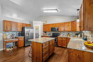 Kitchen featuring appliances with stainless steel finishes, brown cabinetry, a center island, lofted ceiling, and backsplash