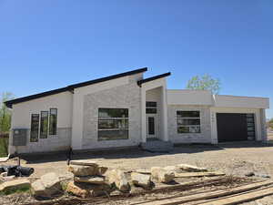 Contemporary home with a garage, dirt driveway, stucco siding, and stone siding