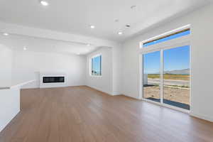 Unfurnished living room with light wood finished floors, a mountain view, baseboards, and a glass covered fireplace