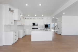 Kitchen featuring light wood finished floors, glass insert cabinets, a kitchen island with sink, appliances with stainless steel finishes, and recessed lighting