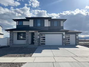 Prairie-style house with a garage, stucco siding, driveway, and stone siding