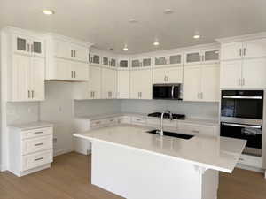 Kitchen featuring a center island with sink, light wood-type flooring, a sink, stainless steel appliances, and recessed lighting