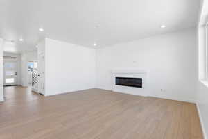 Unfurnished living room with recessed lighting, stairway, light wood finished floors, baseboards, and a glass covered fireplace