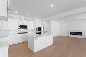 Kitchen featuring white cabinets, light wood finished floors, light countertops, and stainless steel microwave