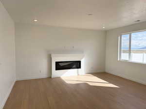 Unfurnished living room with visible vents, wood finished floors, baseboards, a glass covered fireplace, and recessed lighting