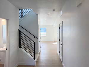 Corridor featuring a textured ceiling, visible vents, light wood-type flooring, stairway, and baseboards