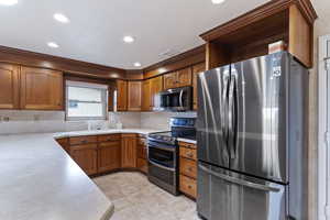 Kitchen featuring appliances with stainless steel finishes, a sink, light countertops, brown cabinetry, and tasteful backsplash