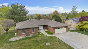 Ranch-style house featuring a shingled roof, brick siding, a garage, a front yard, and driveway