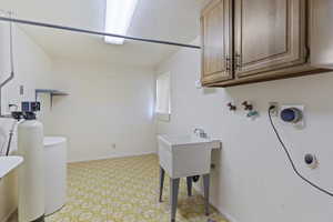 Clothes washing area with light floors, baseboards, washer hookup, and cabinet space