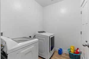 Laundry area with baseboards, light wood-style floors, laundry area, and washing machine and dryer