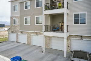 Back of house featuring stucco siding, a garage, driveway, stone siding, and central AC