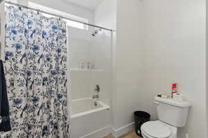 Full bathroom with toilet, shower / bathtub combination with curtain, wood finished floors, and baseboards