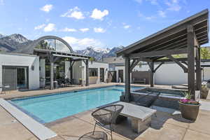 Outdoor heated pool featuring a gazebo covered hot tub, mountain view, and patio