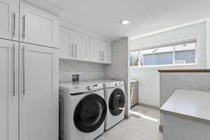Laundry area featuring cabinet space, separate washer and dryer, wallpapered walls and bathroom with sink and toilet, tile floors