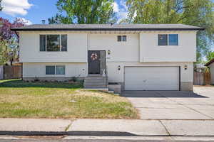 Bi-level home featuring a garage, fence, a front yard, brick siding, and concrete driveway