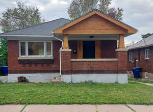 View of front of house featuring a chimney, a porch, a front lawn, and brick siding
