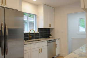 Kitchen featuring a sink, appliances with stainless steel finishes, tile backsplash, and white cabinetry