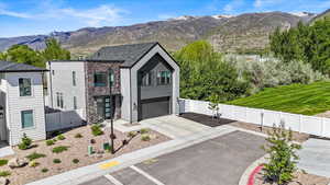 View of front of home with a garage, fence, a mountain view, concrete driveway, and stone siding