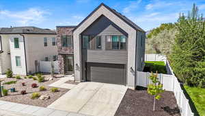 Modern home with fence, stone siding, a garage, stucco siding, and driveway