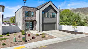 Contemporary house with fence, an attached garage, stone siding, a mountain view, and driveway