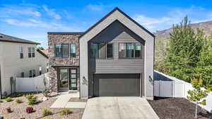 Modern home featuring fence, a gate, driveway, and stone siding
