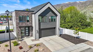 Modern home featuring a garage, fence, stone siding, concrete driveway, and a mountain view