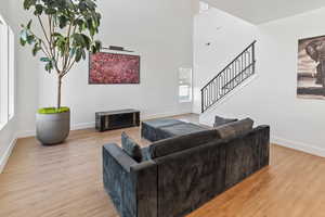 Living room with baseboards, light wood-style flooring, a high ceiling, and stairway