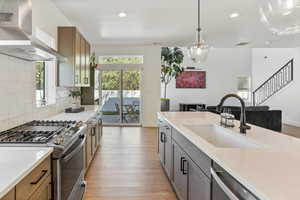 Kitchen featuring visible vents, a sink, light countertops, stainless steel appliances, and wall chimney exhaust hood