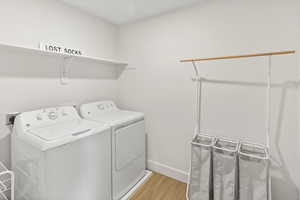 Clothes washing area with baseboards, laundry area, light wood-style flooring, and washer and clothes dryer