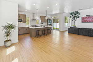 Kitchen with open floor plan, wall chimney range hood, a kitchen bar, stainless steel microwave, and tasteful backsplash
