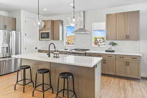 Kitchen with appliances with stainless steel finishes, light wood-type flooring, a sink, a breakfast bar, and wall chimney exhaust hood