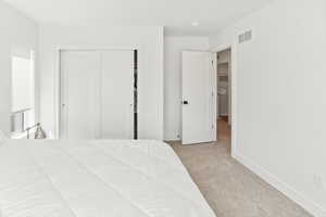 Carpeted bedroom featuring visible vents, baseboards, and a closet