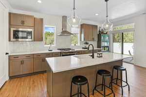 Kitchen featuring wall chimney range hood, light wood-type flooring, light countertops, a sink, and appliances with stainless steel finishes