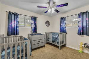 Carpeted bedroom with baseboards, a crib, and ceiling fan