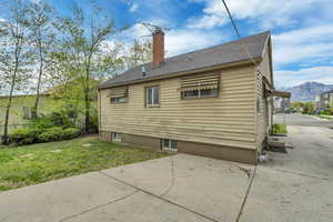 Rear view of property with a patio, roof with shingles, a chimney, a lawn, and a mountain view